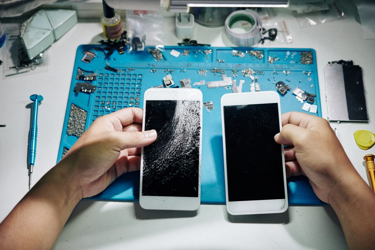 Hands of repairman exchanging smartphone screen with many cracks with the new one